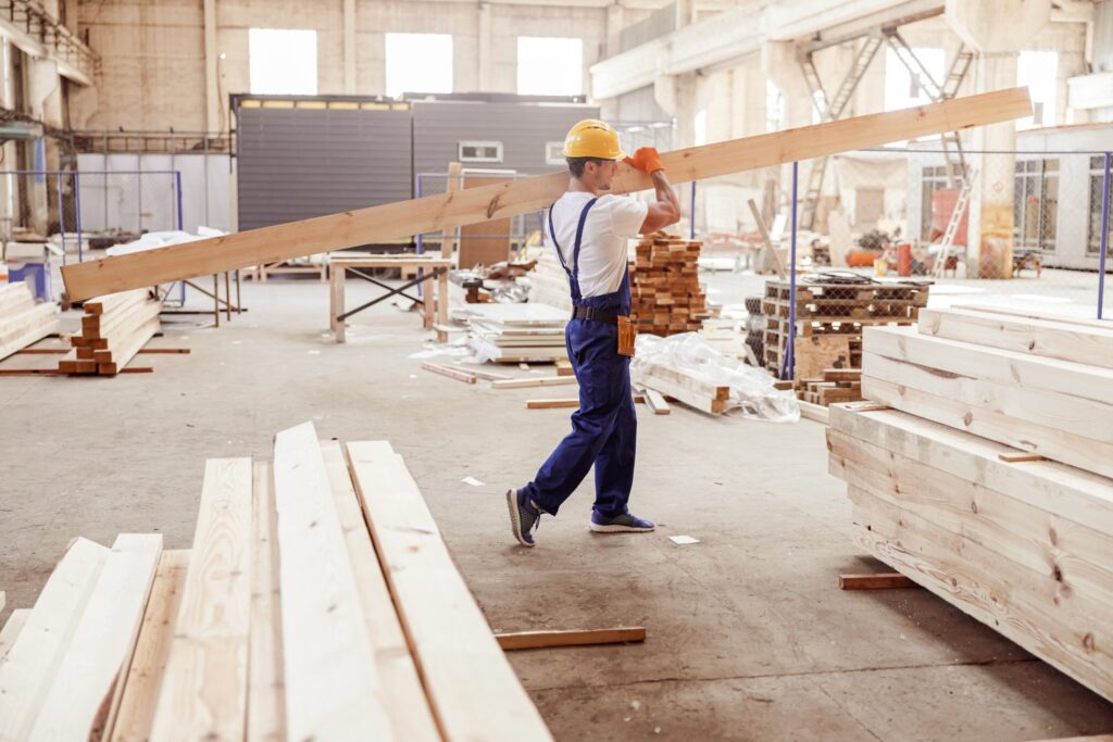 Budowniczy niosący drewnianą deskę w fabryce domów modułowych