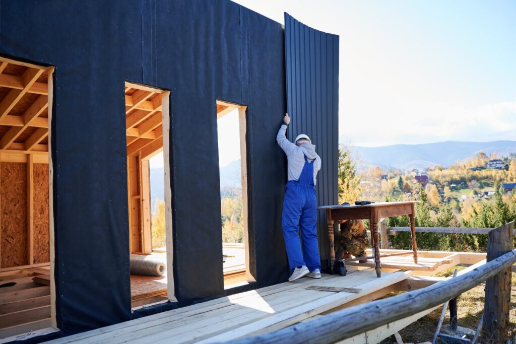 Mężczyzna instalujący blachę falistą używaną jako fasada przyszłego domu prefabrykowanego