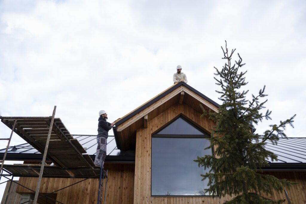 Mężczyźni pracujący razem na dachu drewnianego domu modułowego