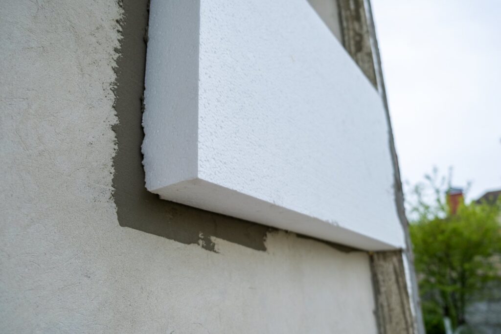 Montaż styropianowych płyt izolacyjnych na ścianie elewacji domu prefabrykowanego w celu zabezpieczenia termicznego