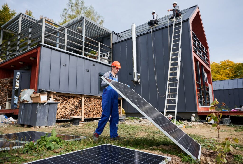 Technicy przenoszący moduł fotowoltaiczny podczas instalowania systemu paneli słonecznych na dachu domu z projektu