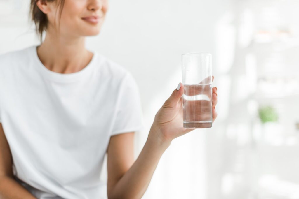 Uśmiechnięta dziewczyna trzyma szklankę zmiękczonej wody rano